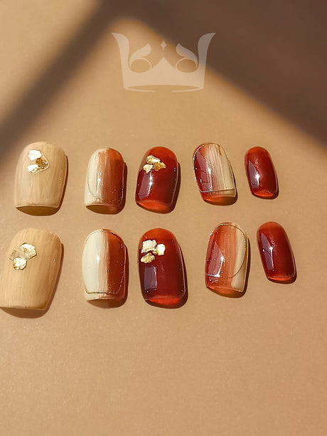 These fall-themed nails have a warm color palette, gold leaf accents, varying sizes, and a versatile design suitable for casual or formal occasions.