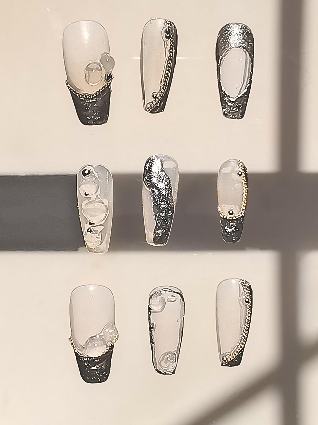 Stylish nails with monochromatic color scheme, gold embellishments, patterns, textures, and trendy designs for fashion statement or special occasion.
