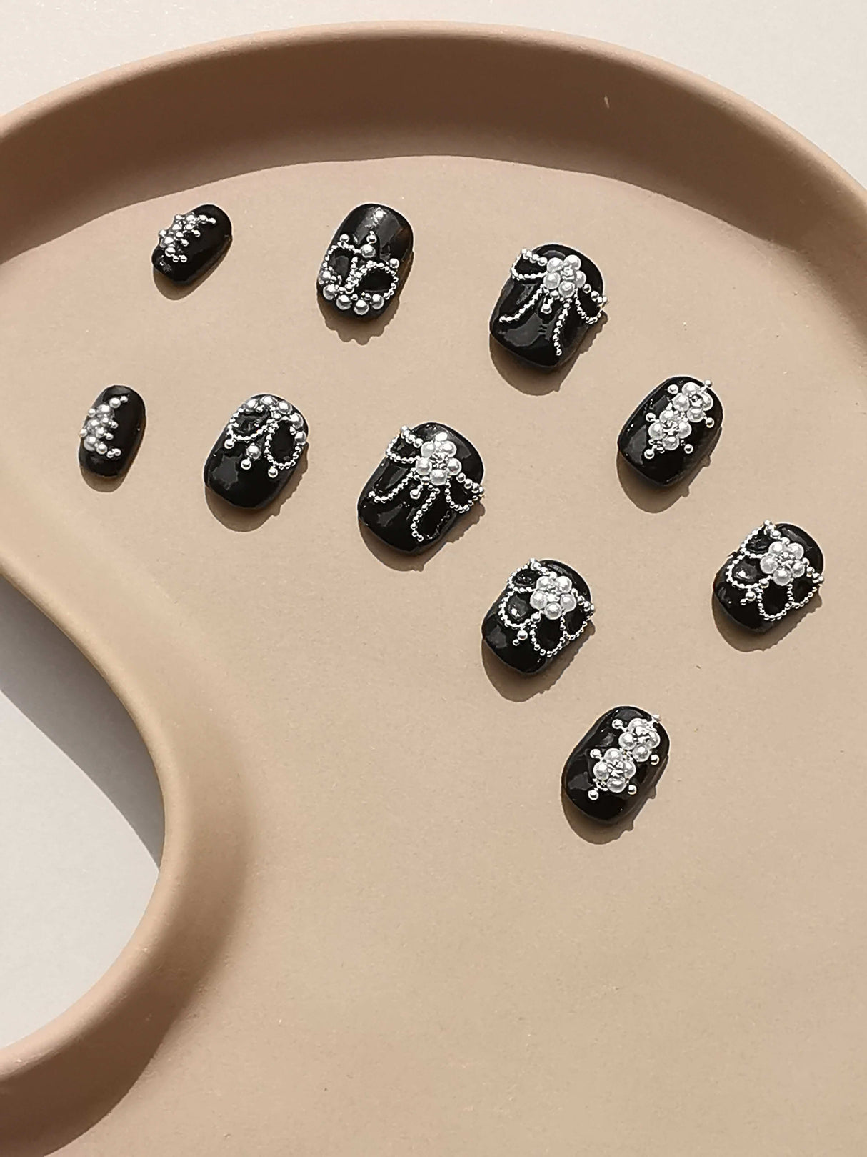 Luxurious and ornate nails with white designs, pearls, and rhinestones for a classic and elegant look. Varying sizes for a full set manicure. Ideal for formal events.