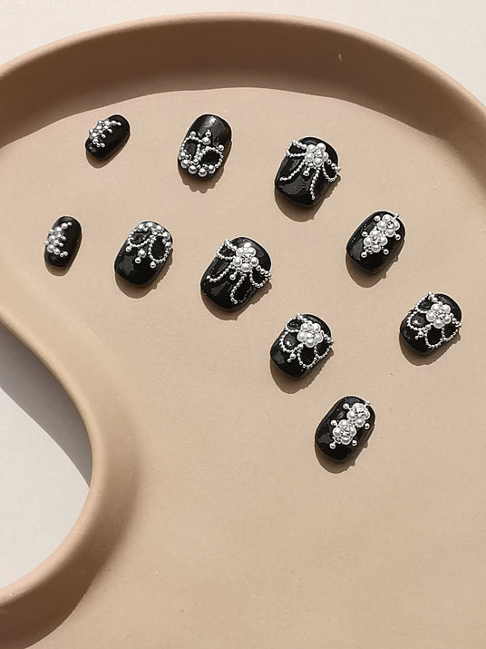 Luxurious and ornate nails with white designs, pearls, and rhinestones for a classic and elegant look. Varying sizes for a full set manicure. Ideal for formal events.