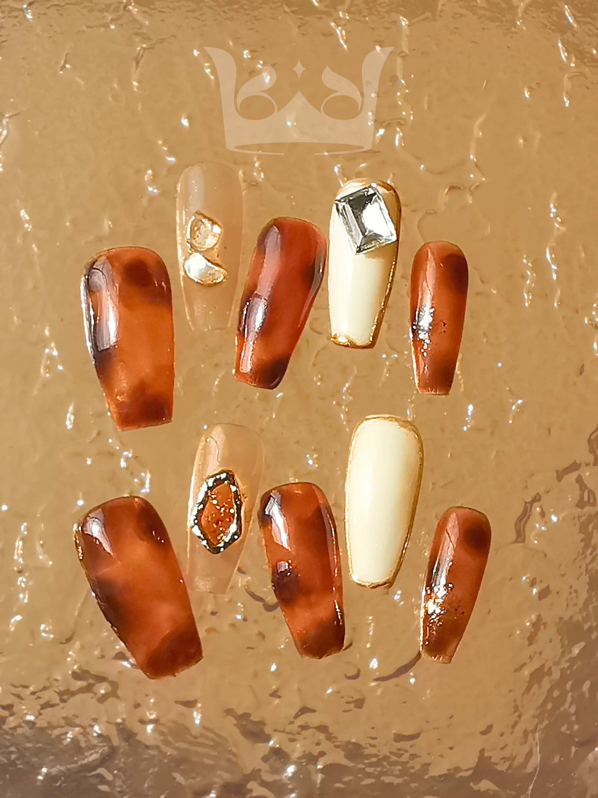 Sophisticated nails with warm tones and ornamental gems for special occasions or photoshoots. Unique design with glossy finish and brown/cream color palette.