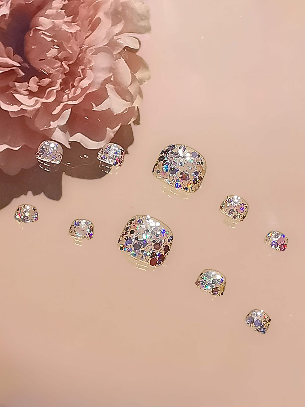 Glittery and sequin-like nails for special occasions or visual media, with a clear/translucent base and displayed against a neutral background for maximum shine.