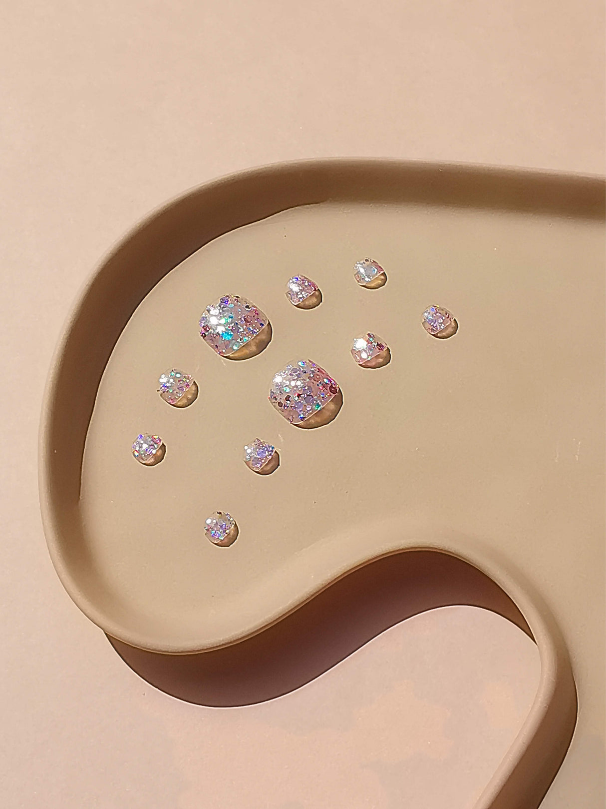 Gemstone nails with iridescent quality arranged elegantly on a smooth surface. Minimalistic design with synthetic/treated diamonds reflecting a spectrum of colors.