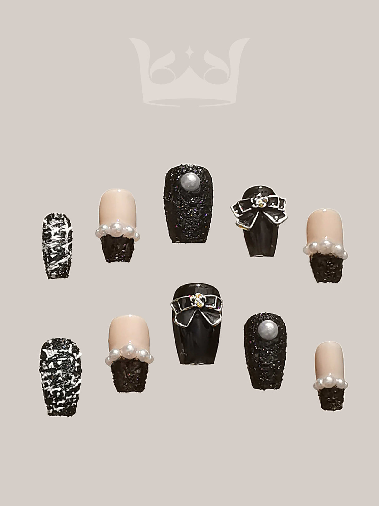 These press-on nails feature a fancy design with black and nude tones, glittery texture, pearls, and metallic accents. The rounded or oval tip shape adds a natural touch.