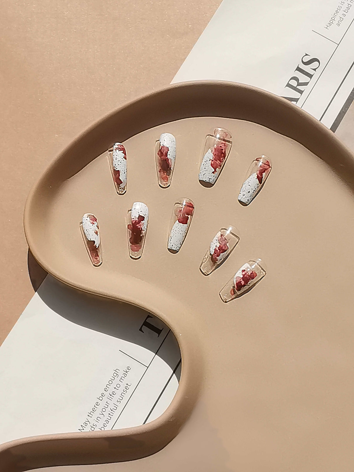 These press-on nails are for fashion-forward individuals. The design is artistic and modern, with a clear base and splatter or marbling effect in white and red.
