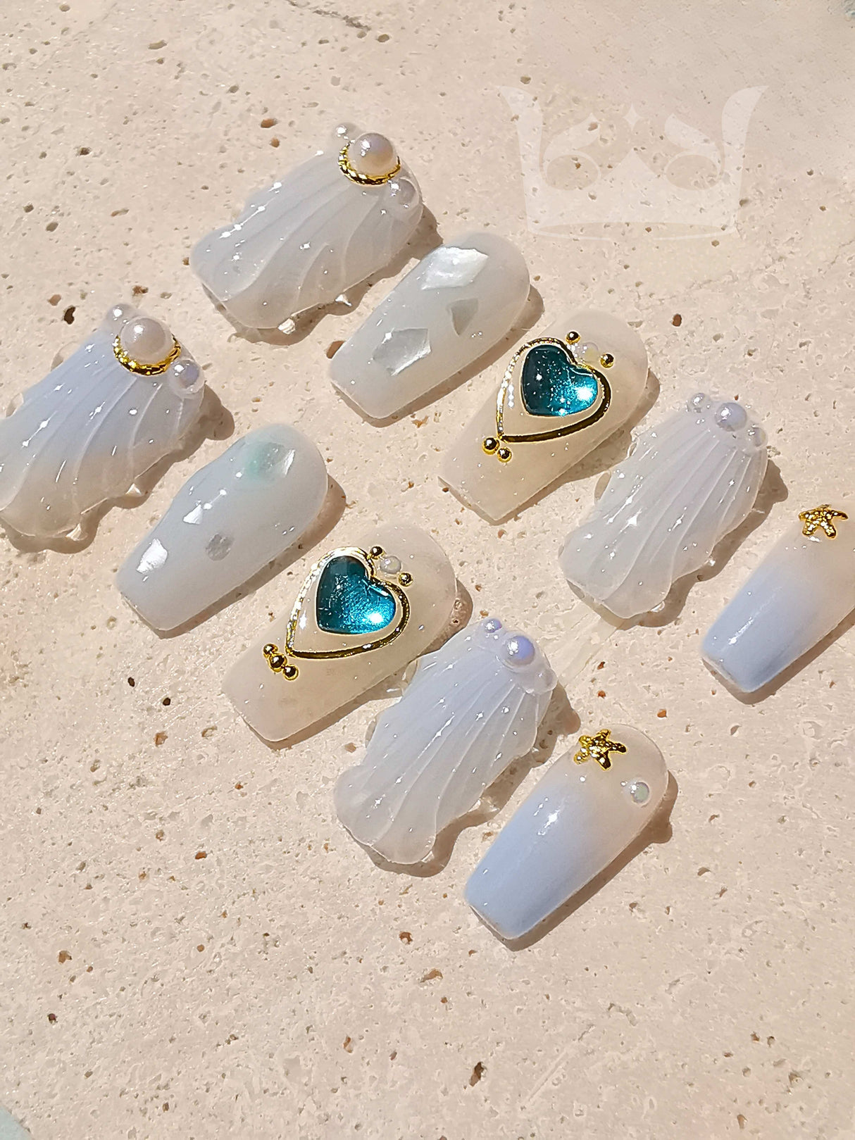 Luxury nail tips with white/translucent base, gold accents, pearls, and heart-shaped blue glittery embellishment for fancy look on special occasions.