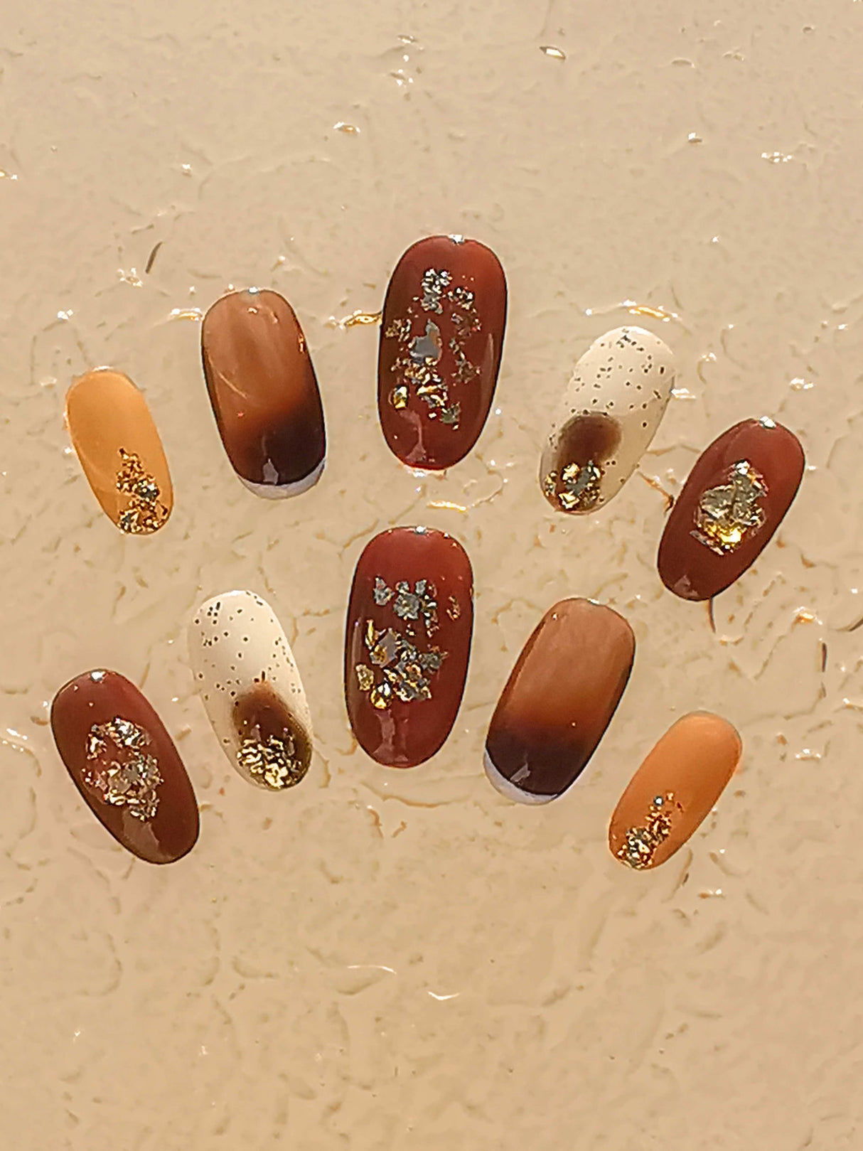 These press-on nails are  for cute purposes, with a warm color scheme, golden floral patterns, and varying lengths. They are ideal for formal events or personal expression.