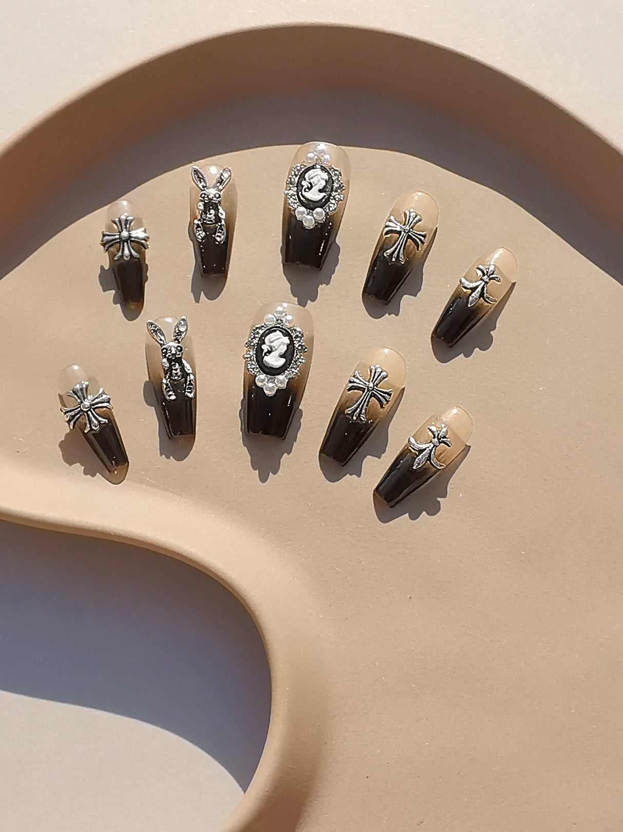 Elaborate black and nude nails with trendy patterns resembling jewelry or cute art, suitable for special occasions or fashion statements.
