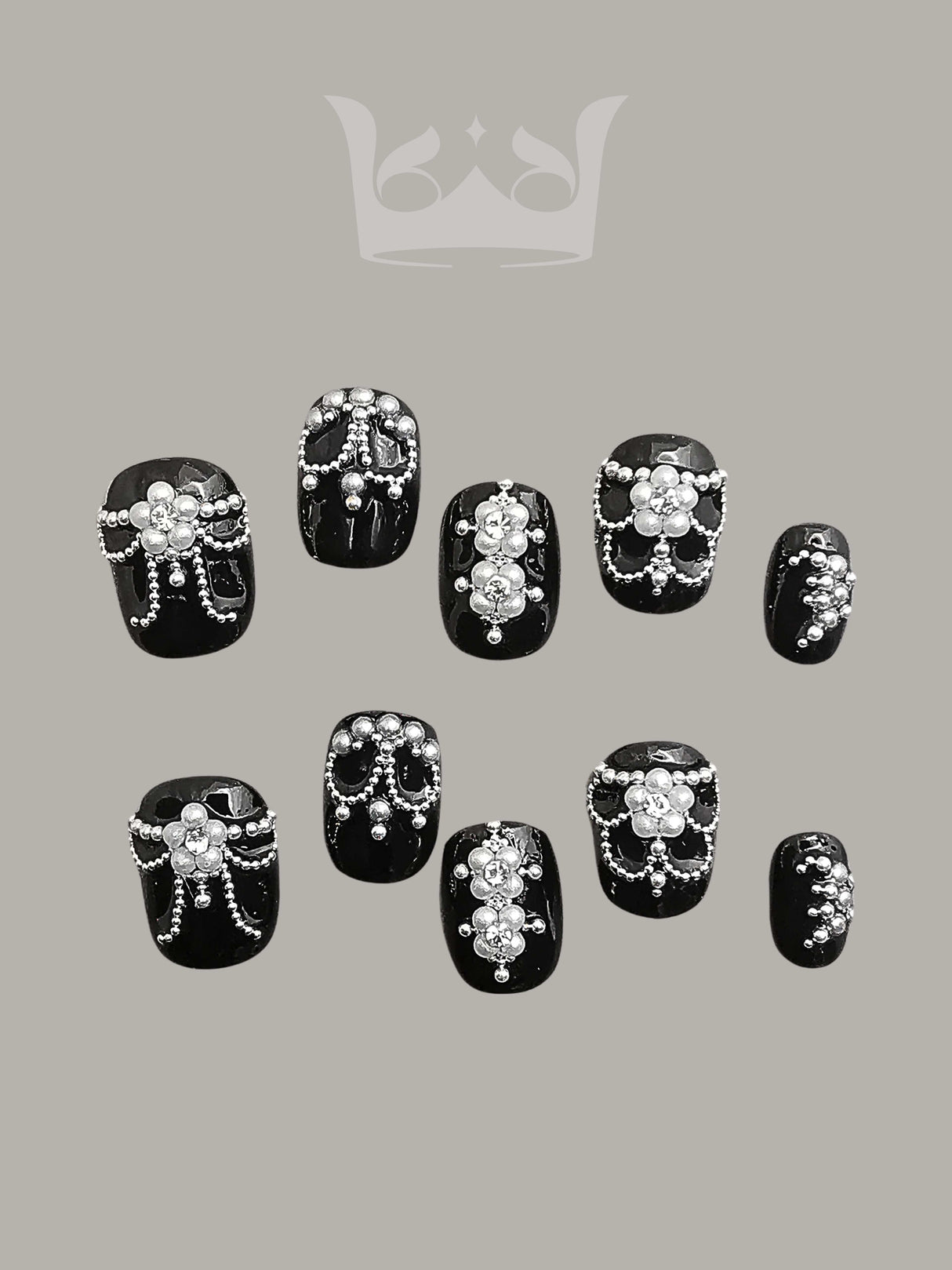 Opulent and ornate nails for special occasions with black base, white pearls, silver rhinestones, floral motifs, and varying sizes for customization.