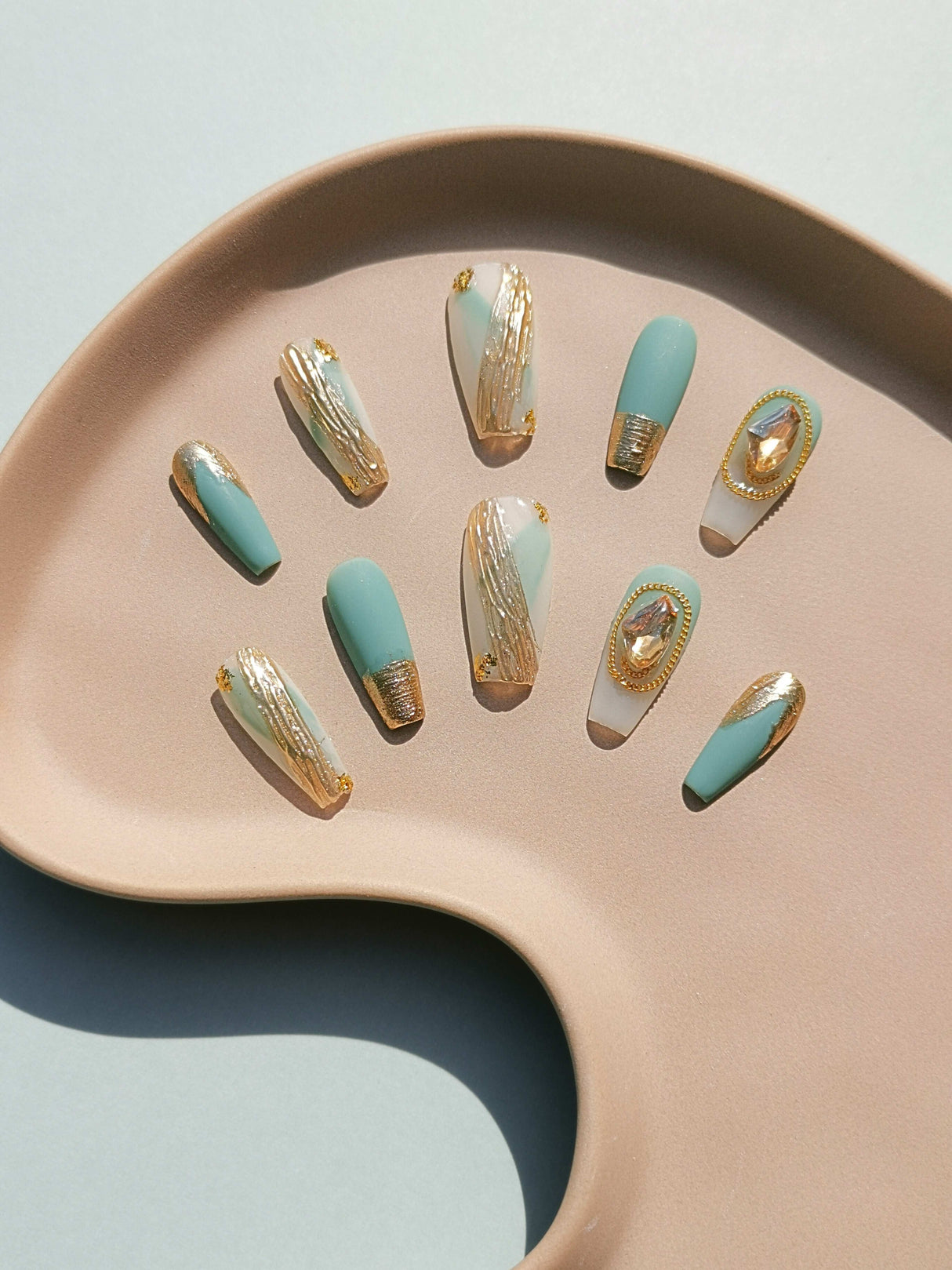 These press-on nails are designed for a fashionable and formal occasion, featuring a combination of modern and art deco elements with a seafoam green and metallic gold color scheme. 