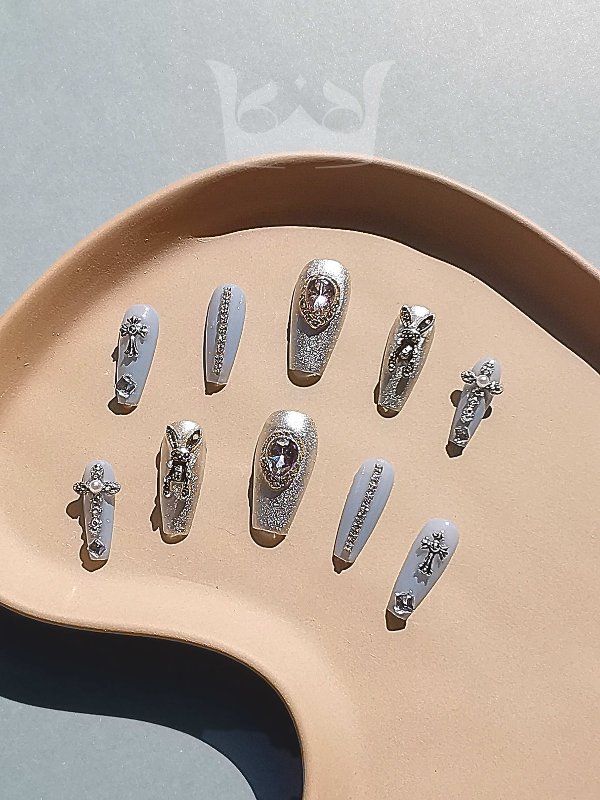 These press-on nails have a glamorous and trendy design with metallic silver base color, clear rhinestones, detailed artwork, and accent nails, suitable for special occasions.