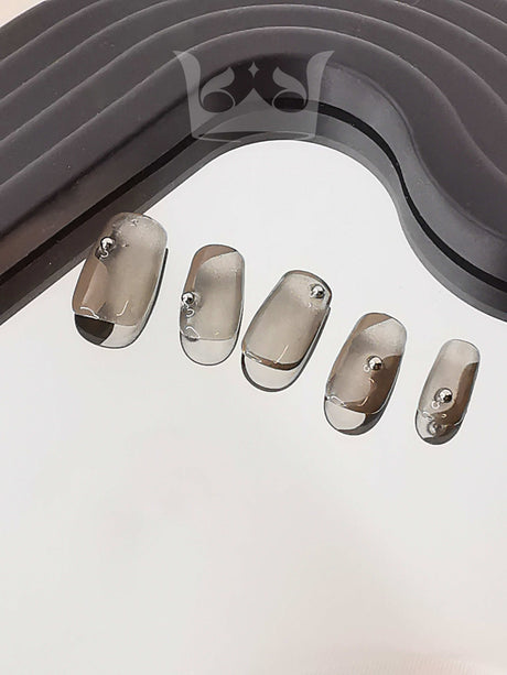 Clear acrylic nails with size gradient and metal studs for minimalist and modern nail art design. Purpose of gray object unclear. Intended use unknown.