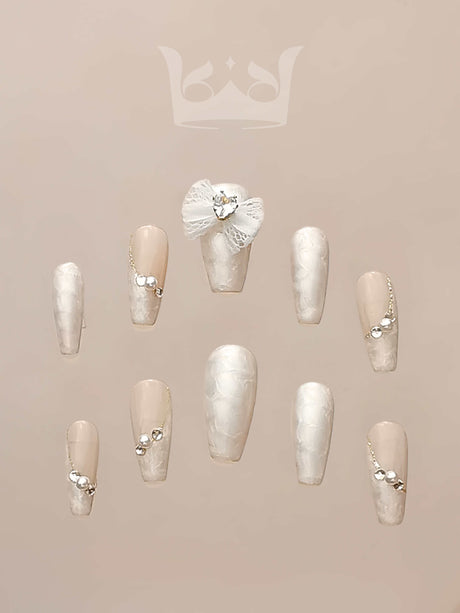 Luxurious and fancy nails with neutral base color, white marble effect, small embellishments, delicate chains, and 3D floral design for special occasions.