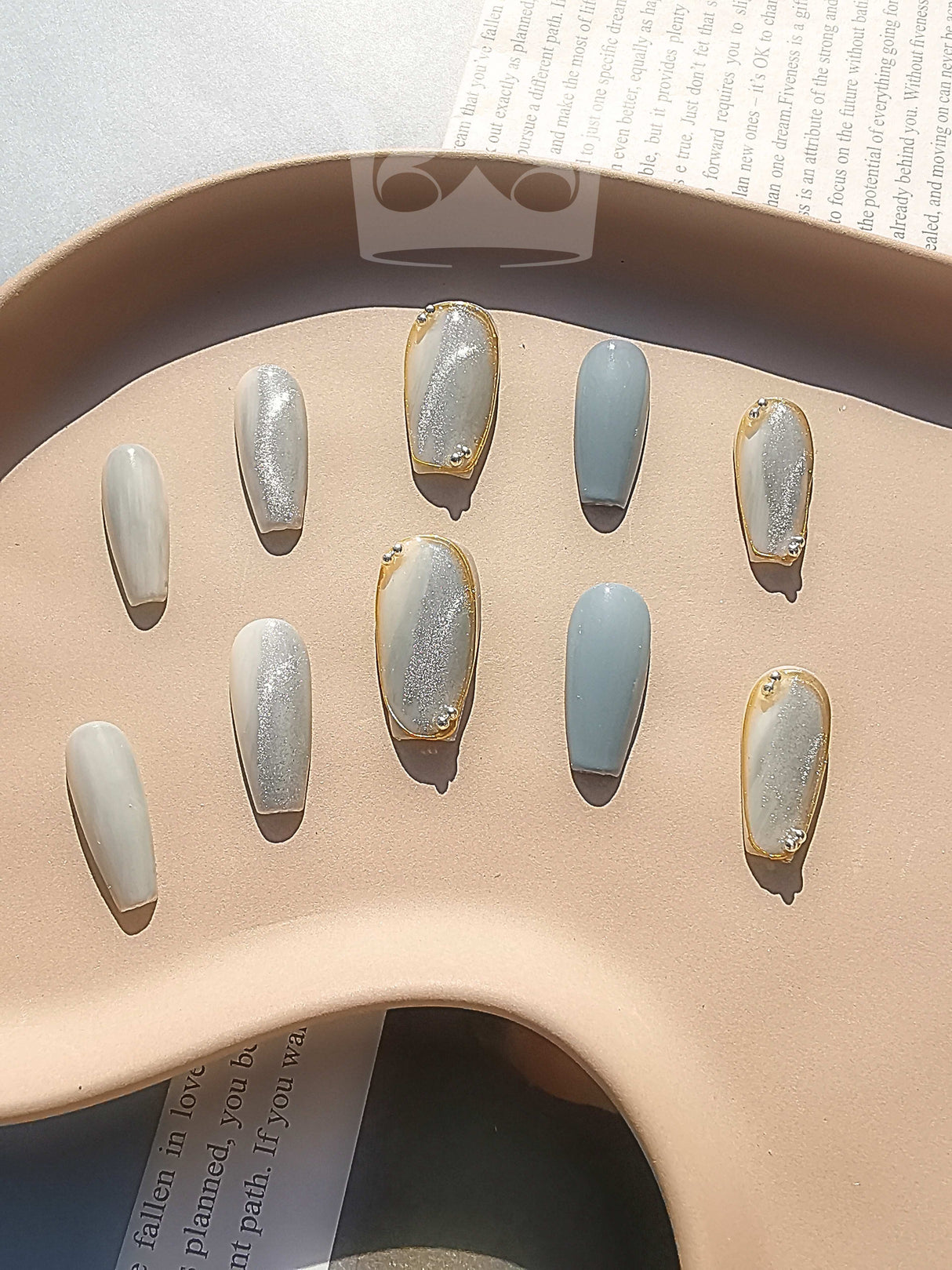 These press-on nails are designed for special occasions or fashion statements with a soft color palette, oval shape, two-tone design, metallic accent, gold detailing, and texture contrast.