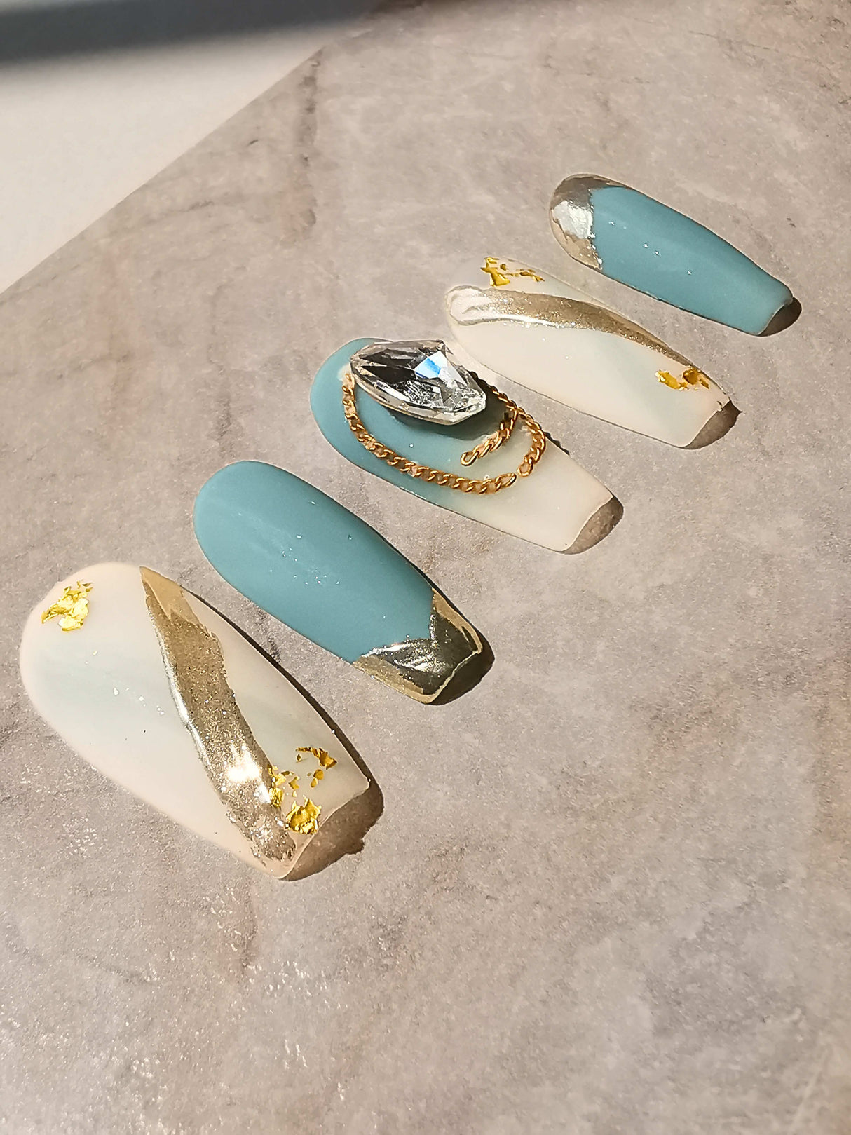 Luxurious and cute nails with a dual-color scheme, gold metallic foil accents, rhinestone embellishment, and mix of textures for special occasions.