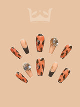 Luxurious tortoiseshell pattern nails with gold foil accents for fashion-forward nail art enthusiasts who appreciate unique designs. Nude base with black and orange splotches.