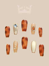 Fashion-forward nails with brown color scheme, marble/tortoiseshell patterns, diamonds, metal settings, and geometric cut-outs for a unique statement.