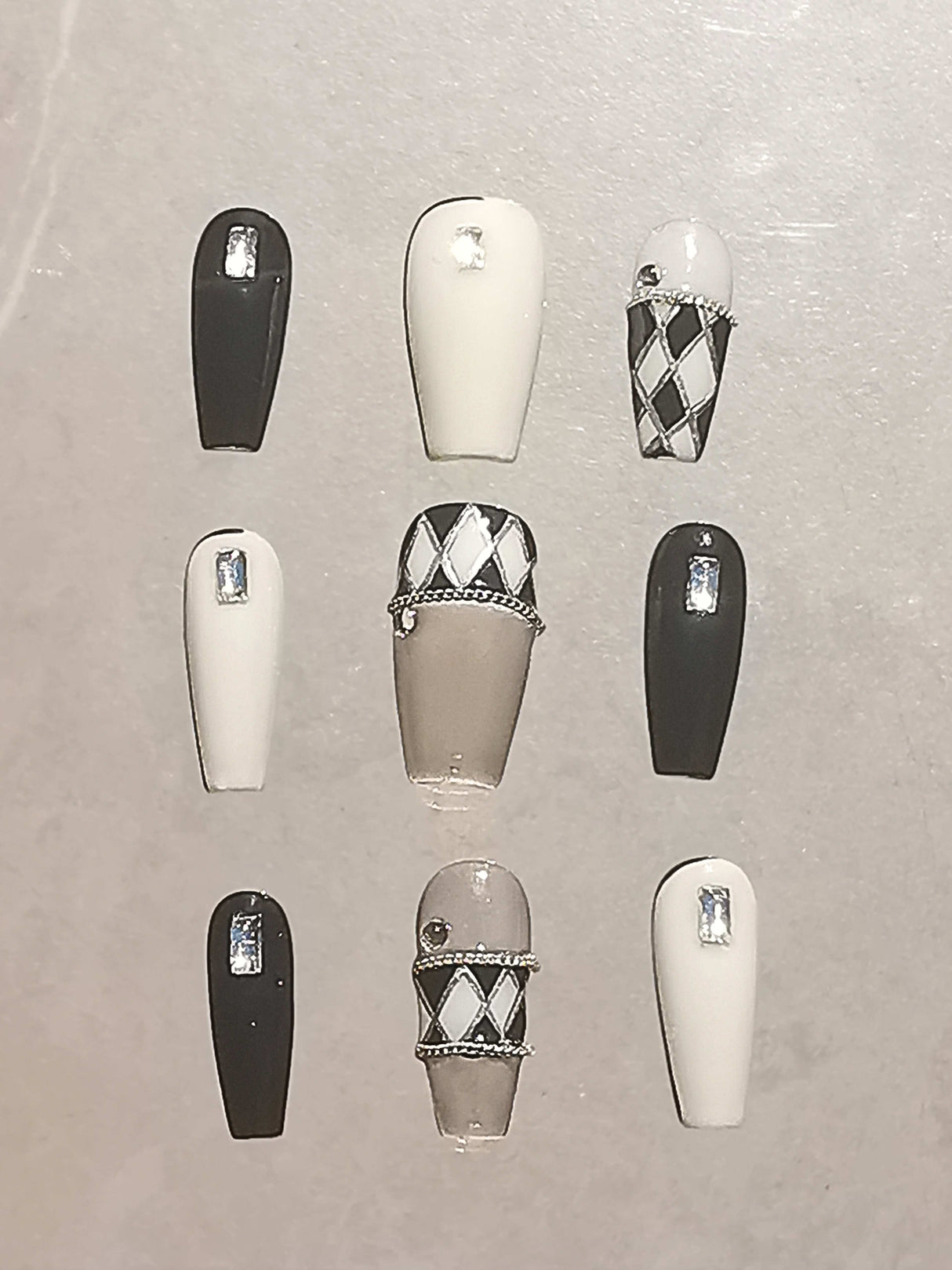 These black and white nails with rhinestones, argyle pattern, chains, and glossy finish are perfect for formal events or fashion statements.