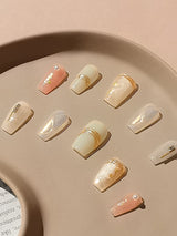 These acrylic nails with a soft, neutral color palette, gold embellishments, and trendy shapes are designed to enhance fashion and style for special occasions.