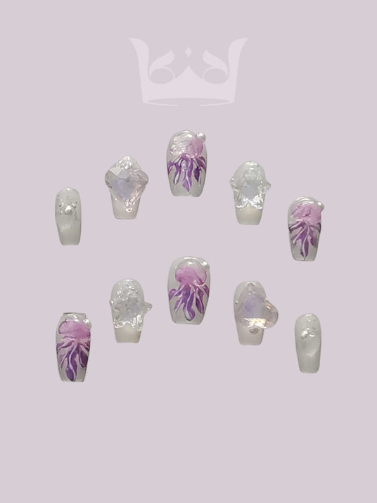 These press-on nails featuring trendy detailing, a white and purple color scheme, hand-painted patterns, and 3D crystal embellishments. They are stiletto shaped with a glossy or textured finish