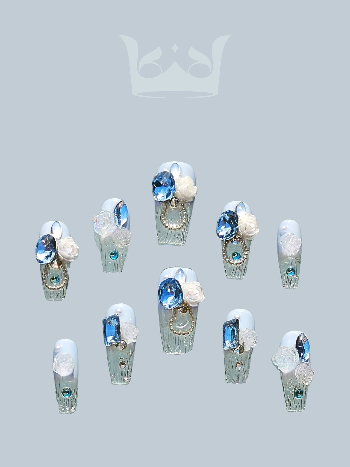 These cute nails with blue diamonds, clear crystals, and white floral accents are designed for a cool and elegant aesthetic with a touch of royalty.
