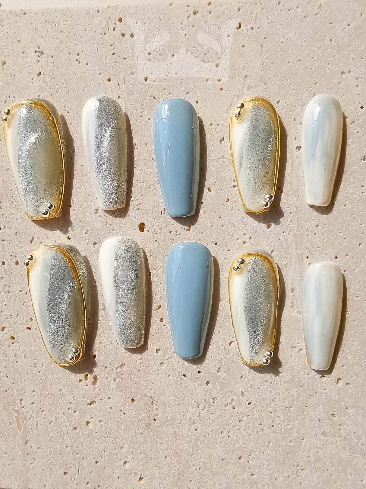 These press-on nails are perfect for a special occasion with a unique design featuring a two-tone effect, gold embellishments, and a coffin/ballerina shape. The glossy topcoat adds a polished finish.