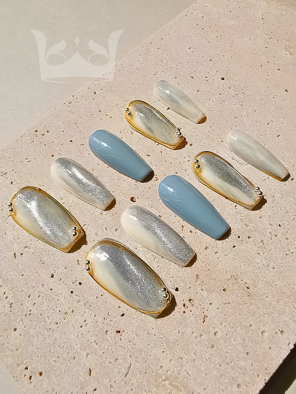 These press-on nails are designed for special occasions or fashion statements with a soft color palette, oval shape, two-tone design, metallic accent, gold detailing, and texture contrast.