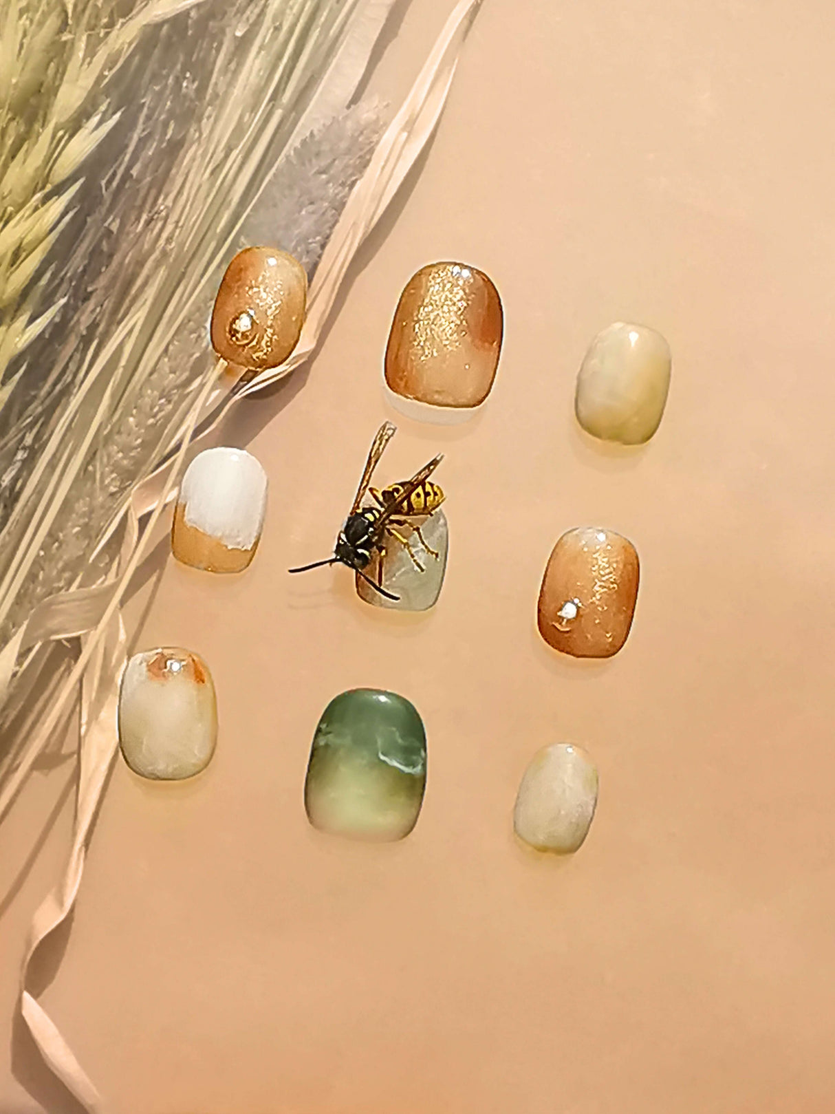 These press-on nails feature earthy colors, metallic accents, and a realistic-looking wasp for a chic and organic look that complements a natural and minimalist fashion style.