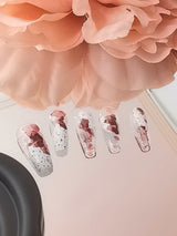 These press-on nails have a clear base, marbled effect, and glitter accents create a trendy appearance suitable for various occasions. The long, tapered shape adds to the overall aesthetic.