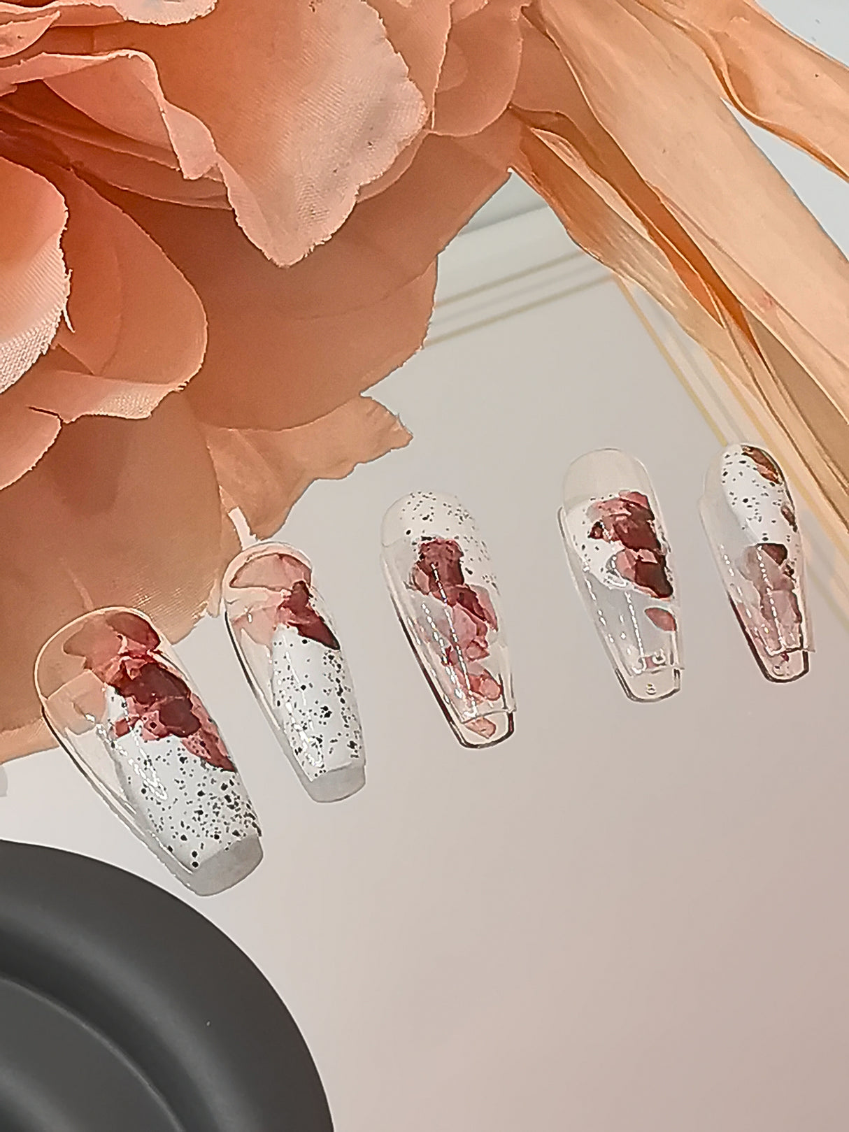 These press-on nail feature a paint-splatter effect in red and black colors, small black speckles for texture. They are long and shaped in a coffin or ballerina style.