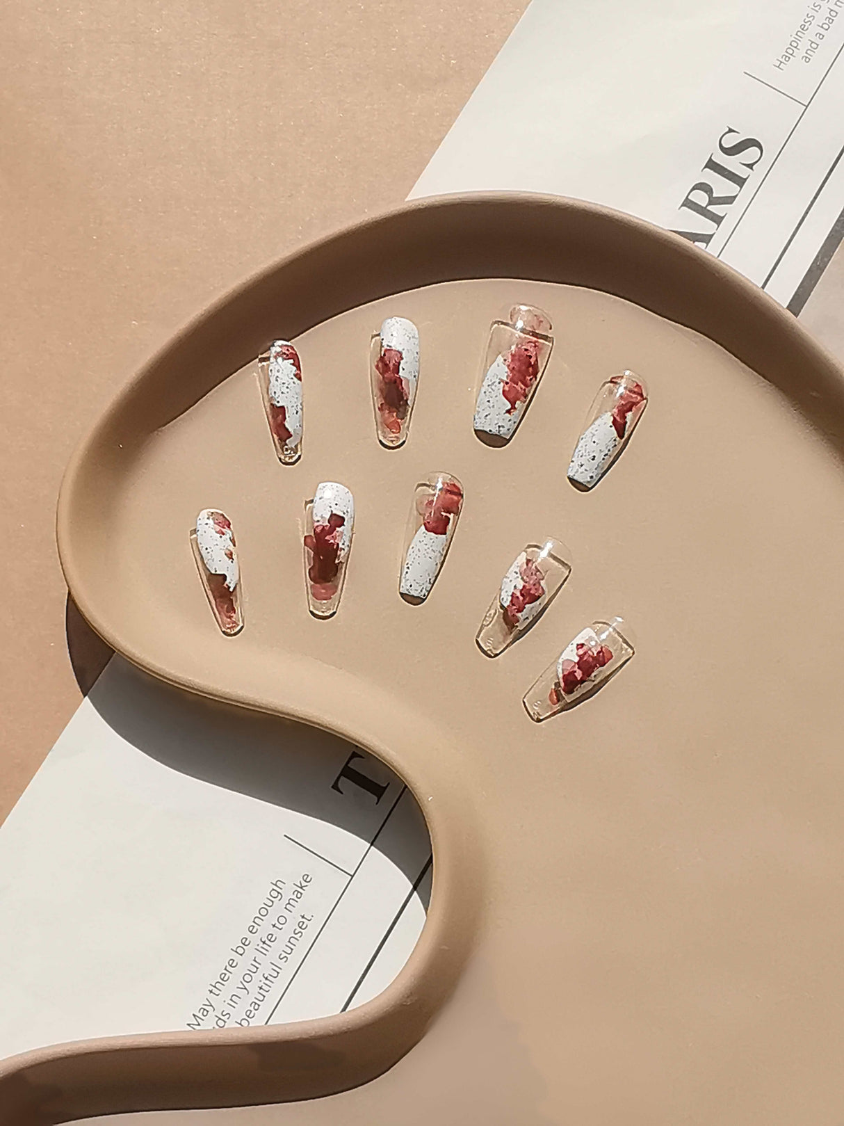 These press-on nails are for fashion-forward individuals. The design is artistic and modern, with a clear base and splatter or marbling effect in white and red. 