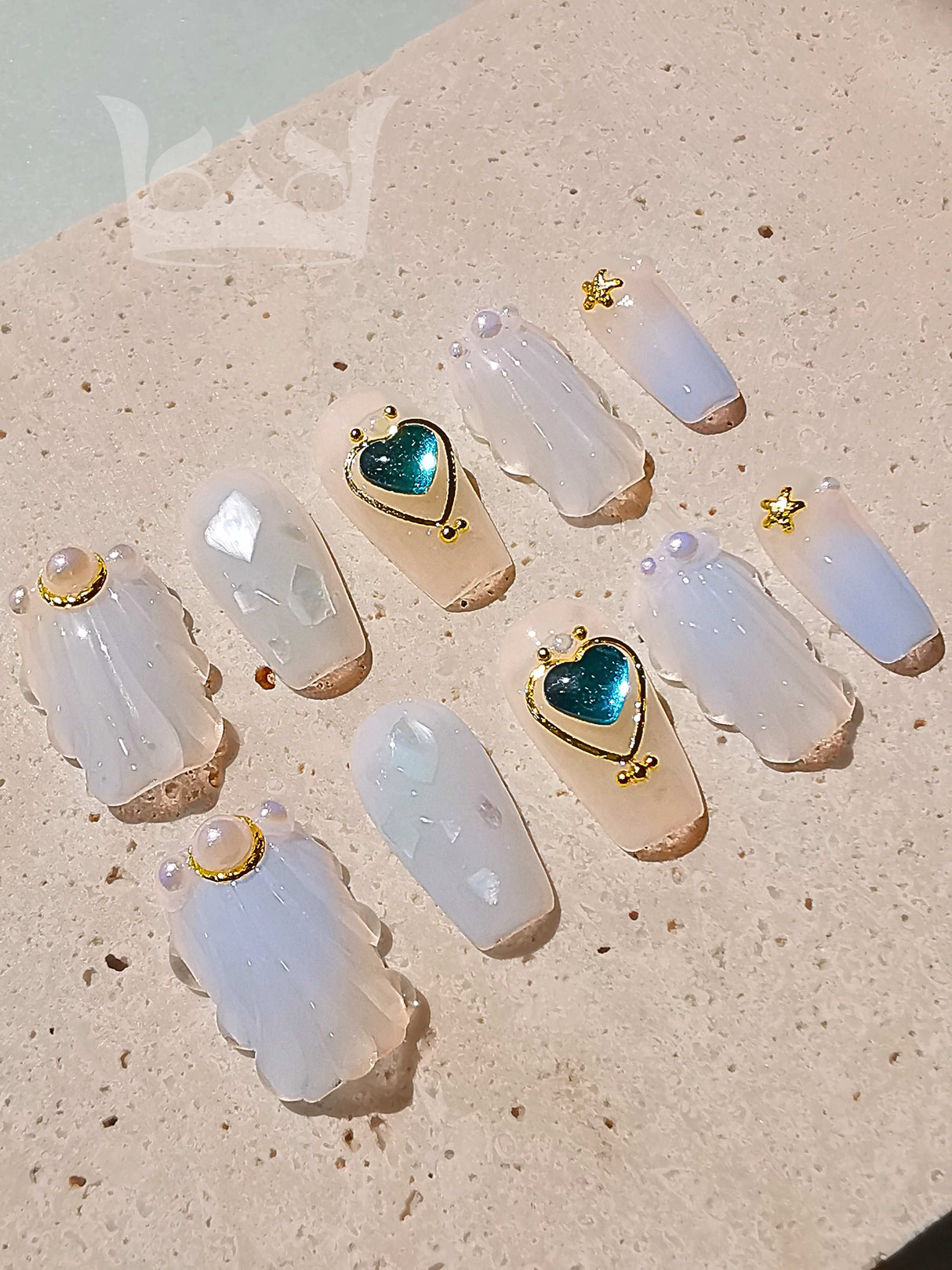 Translucent, milky white acrylic nails with golden accents, stars, and gems for nail art or manicure purposes. Varying sizes and shapes to fit different fingernails.
