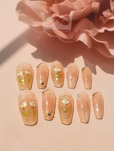 These press-on nails have a subtle yet eye-catching design. They feature delicate floral designs and small gold embellishments, with a clear or nude base color