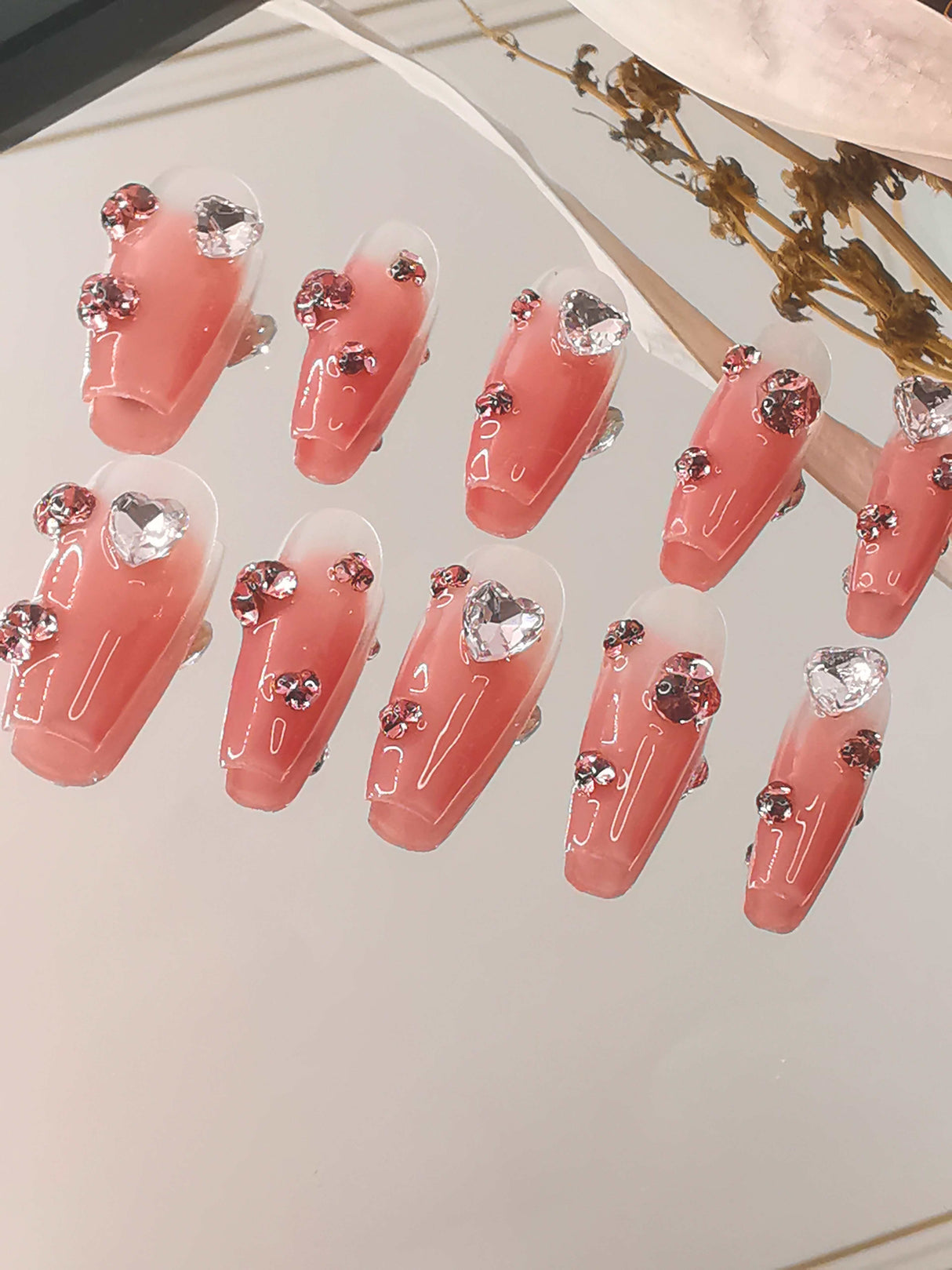 Glamorous and statement-making nails for special occasions with pink ombre effect, large rhinestones, scattered smaller ones, glossy finish, and coffin/ballerina shape.