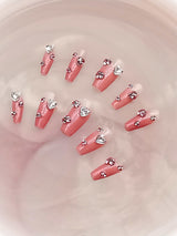 Elegant and glamorous nails with soft pink base, large rhinestone, scattered smaller ones, clear/silver color, medium length, and square/rounded tip.