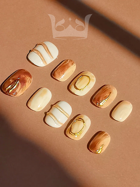 These press-on nails are designed for special occasions, with artistic patterns and gold accents. They come in different sizes and have a neutral background.