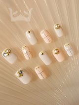 Sophisticated and elegant nails with a pastel pink base, metallic gold lines, gold studs, and clear crystals. Suitable for formal events or everyday wear.