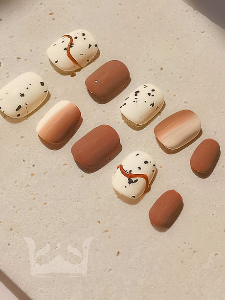 These versatile nails feature a warm, neutral color palette with playful patterns and solid colors, suitable for adding a stylish touch to any outfit.