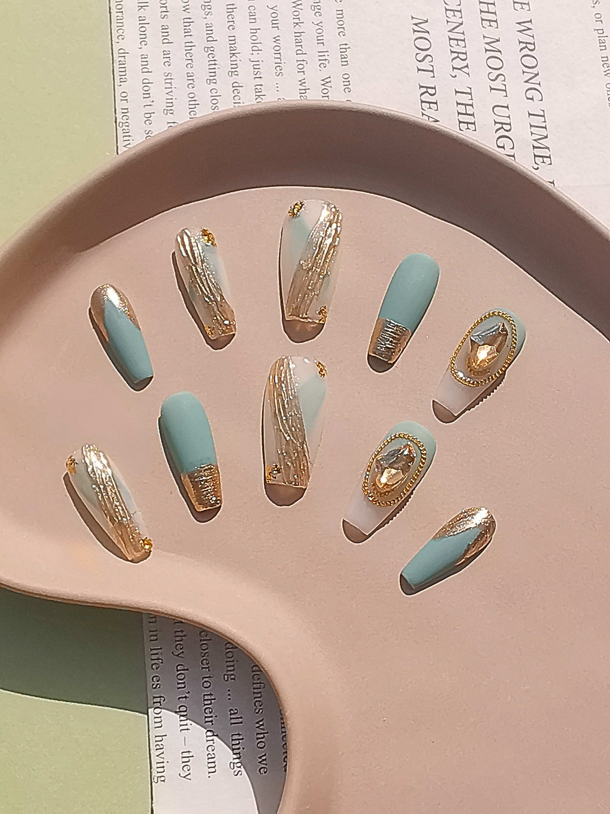 Elaborate and luxurious nails with matte pastel blue color, gold foil/glitter tips, and gold frames with white/clear stones for fashion statements or special occasions.