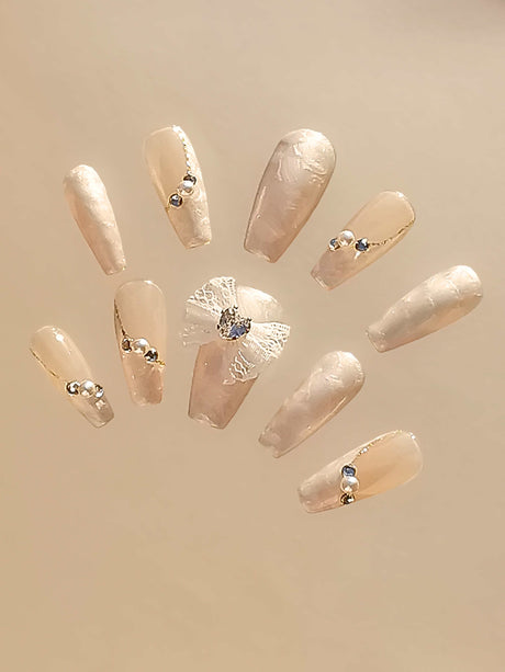 Sophisticated nails for special occasions or statement manicure with neutral/nude base, pearlescent/metallic sheen, rhinestones/crystals, and lace appliqué.