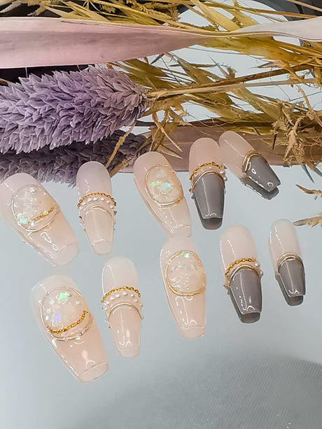 Fashionable nails for special occasions or bold statements. Neutral color palette with gold chains and iridescent flakes. Eye-catching and creative design.